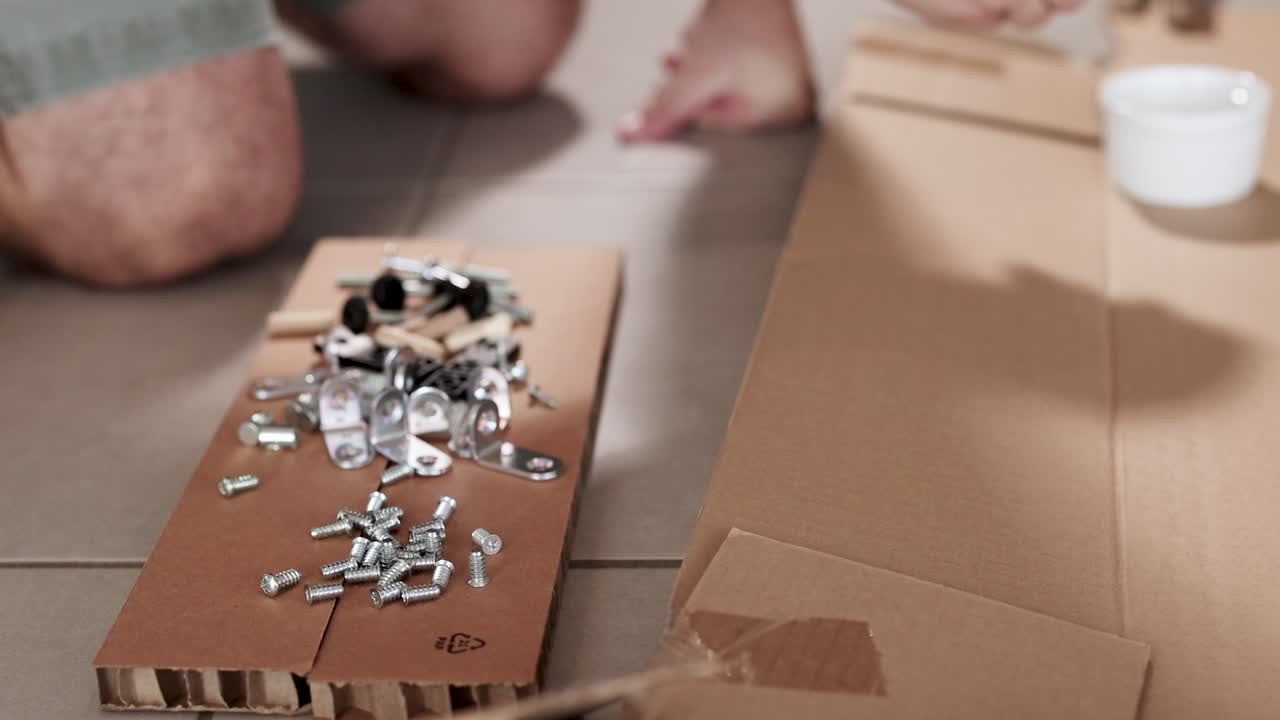 Hands sorting screws and bolts on cardboard in a well-lit room, showcasing a DIY furniture assembly process