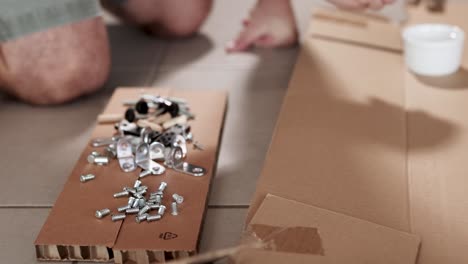 hands sorting screws and bolts on cardboard in a well-lit room, showcasing a diy furniture assembly process