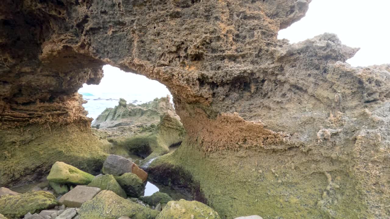 A detailed view of rugged coastal rock formations with natural arches and tidal pools under soft daylight