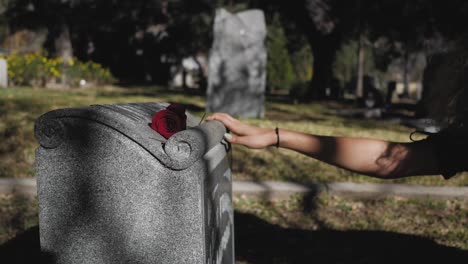 una mujer está parada frente a ti, la tumba de un ser querido, dejando una rosa atrás