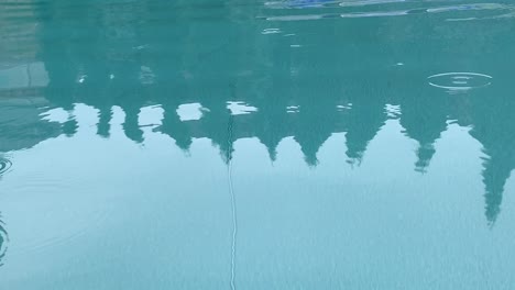 Gotas-De-Lluvia-En-El-Agua-De-La-Piscina-Azul-Con-Reflejo-De-árboles