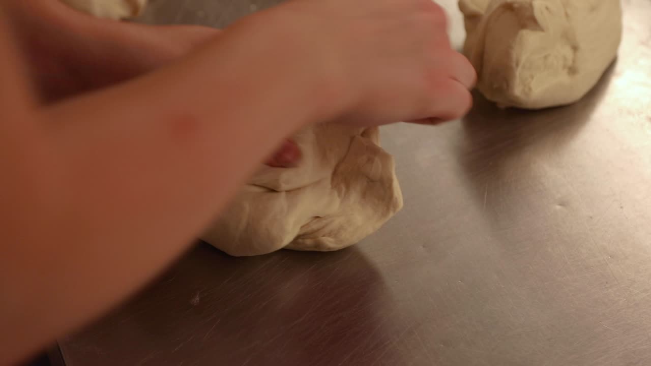 Baker's Hands Kneading Bread Dough On Stainless Tabletop In The Kitchen - close up