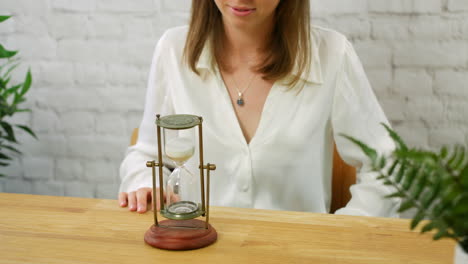 a young woman turning over an hour class egg timer to measure the passing of time