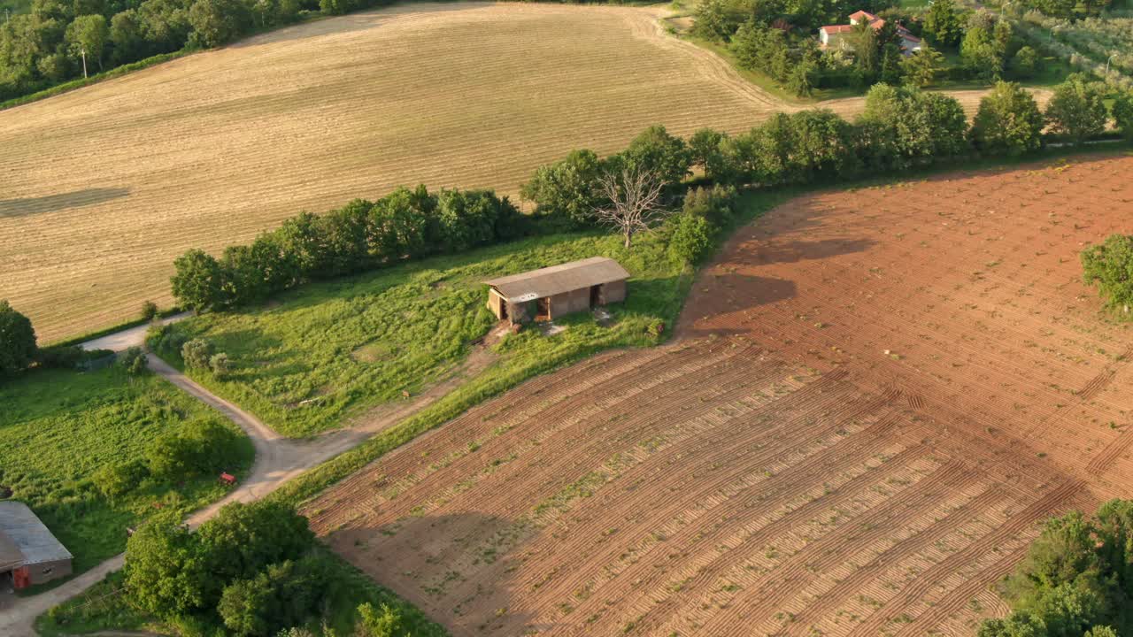 Luftfoto af et lille redskabsskur på landbrugsjord omgivet af marker og skov