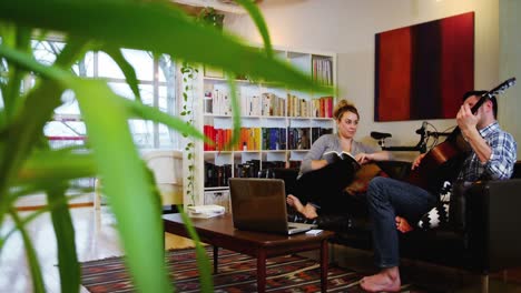 man playing guitar while woman reading book