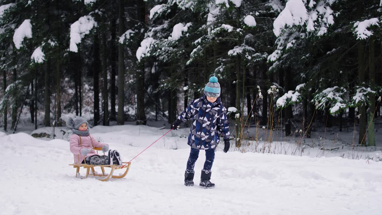 video de hermano tirando de trineo con la hermana pequeña en la nieve