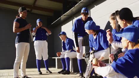 grupo diverso de jugadoras de béisbol y entrenador, entrenador instruyendo a los jugadores en el banco