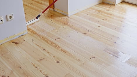 worker applying clear polyurethane varnish to wooden floor using paint roller. high angle shot