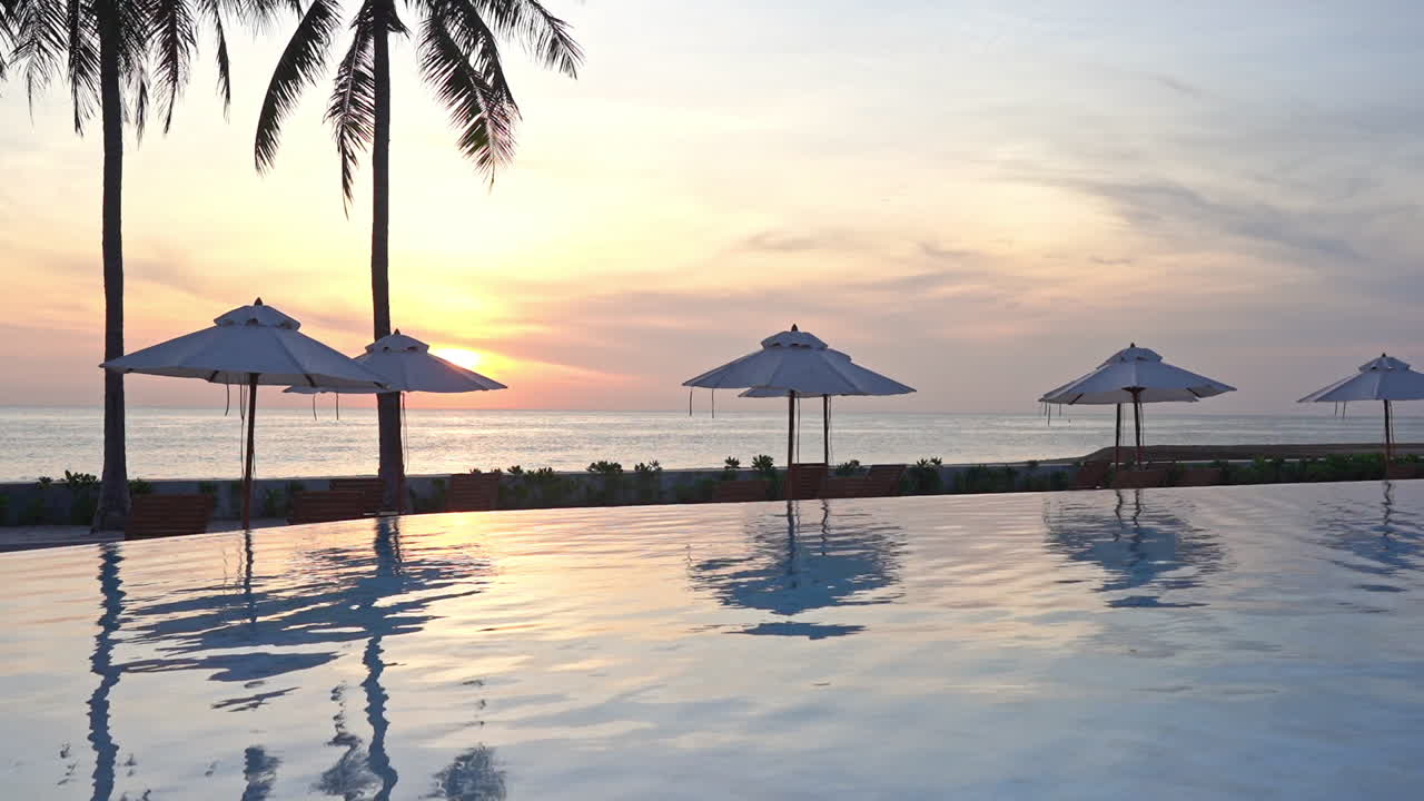 una puesta de sol tropical enmarca las sombrillas de playa con luz rosa, naranja y amarilla