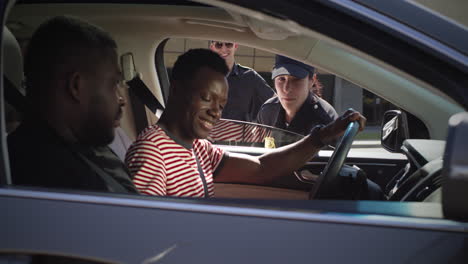 friendly police officer checking digital license of black driver zoom in view of positive woman in police uniform talking with african american man in car and scanning digital driver license on smartphone