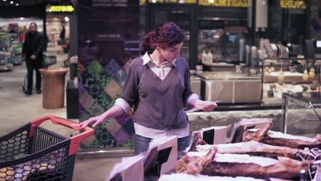 young female buyer picks out some pre-packed meat product in a grocery store