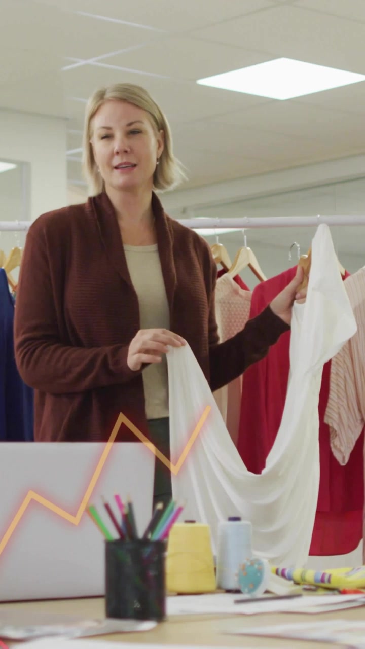 Parlando, tenendo un vestito bianco, donna in cardigan che liscia le cuciture per mostrare la vestibilità in studio, con sovrapposizioni.