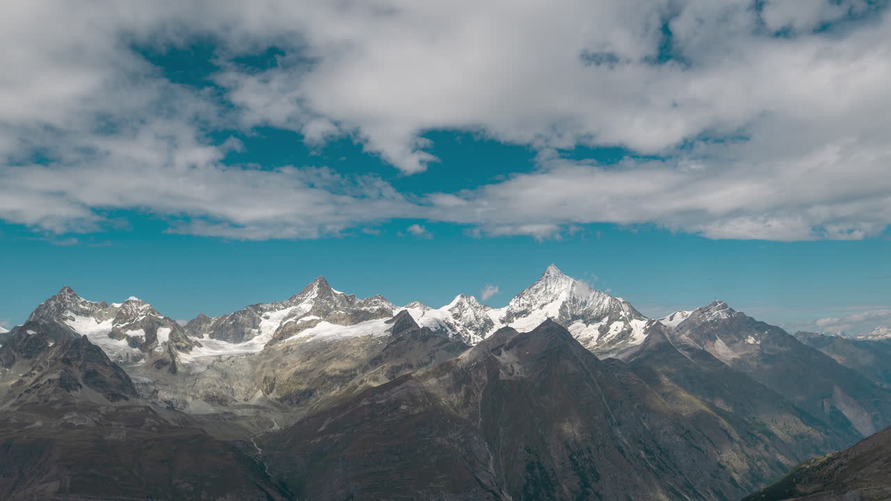 Panoramic view of towering alpine mountains with snow-covered peaks and rugged ridges under a partly cloudy blue sky