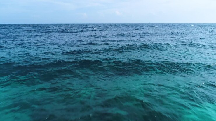 Acqua limpida e ondeggiante dell'Oceano Caraibico con onde dolci e barriera corallina poco profonda sottostante, ripresa aerea con drone in avvicinamento