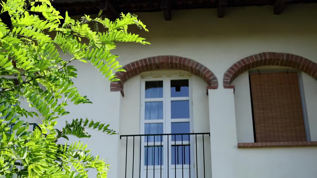 Bright green leaves sway near arched windows with shutters, capturing a serene outdoor scene.