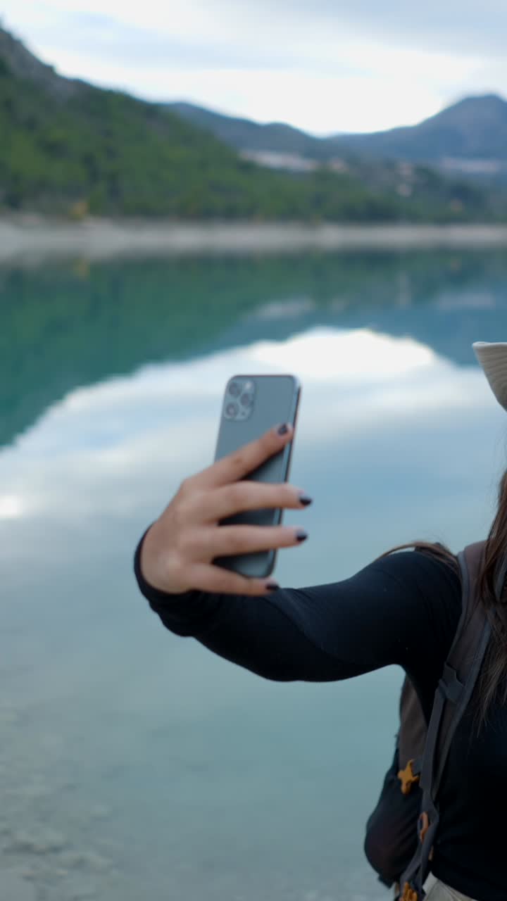 Woman takes a selfie by a scenic lake in the mountains