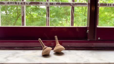 Minimal-wooden-red-frame-window-and-wooden-craft-spinning-top-green-tree-natural-nature-landscape-in-rural-area-village-town-forest-local-people-life-in-Iran-two-couple-kid-child-playing-device-rotate