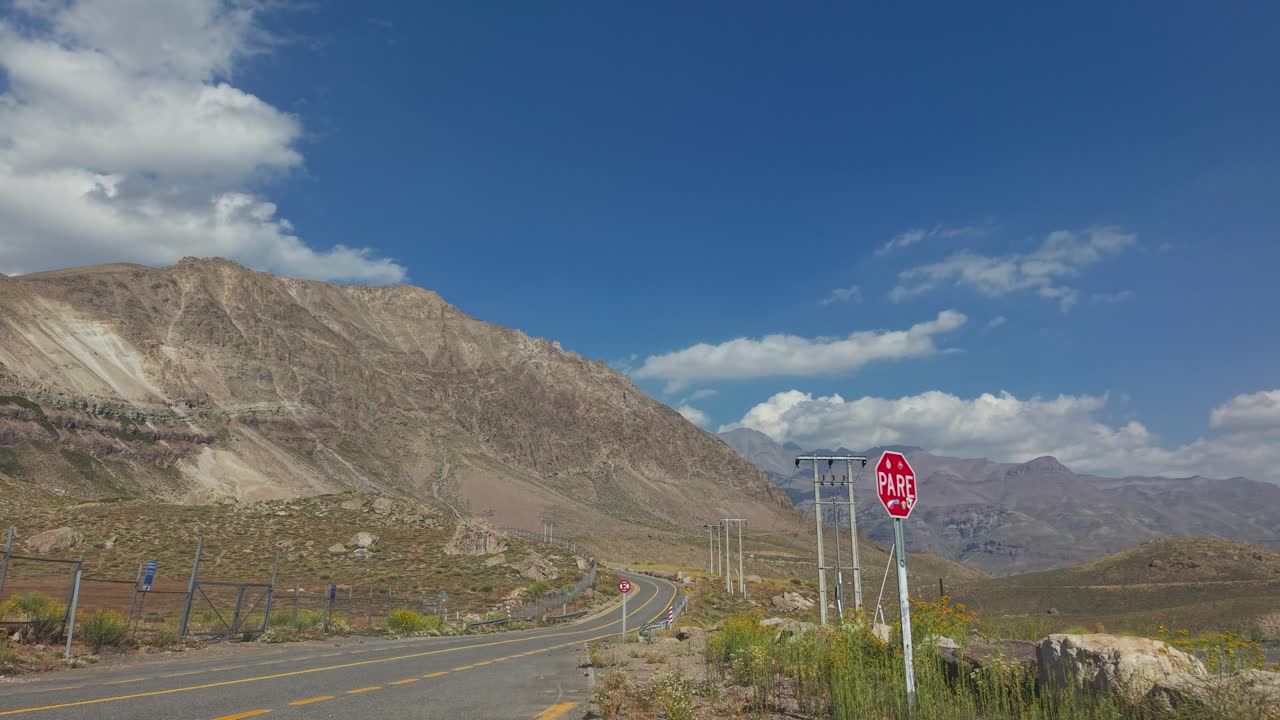 Timelapse di un'autostrada di montagna tortuosa a Farellones con un drammatico terreno andino, segnale di stop a bordo strada e cieli aperti—ideale per viaggi su strada, turismo e riprese documentaristiche. Cile, 4K
