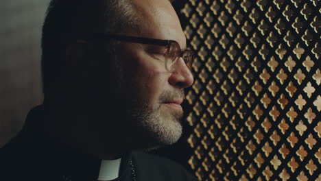 penitent and priest speaking through latticed opening of confessional