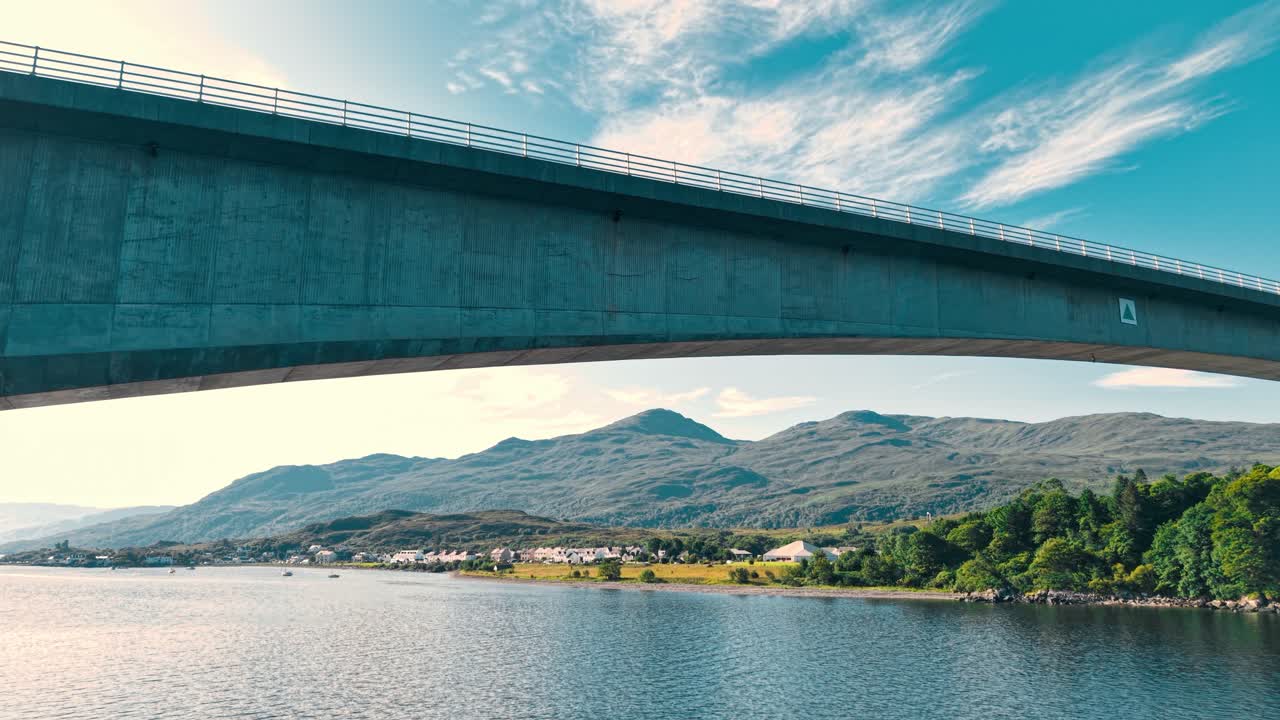 Bridge over a body of water with mountains and a town in the background