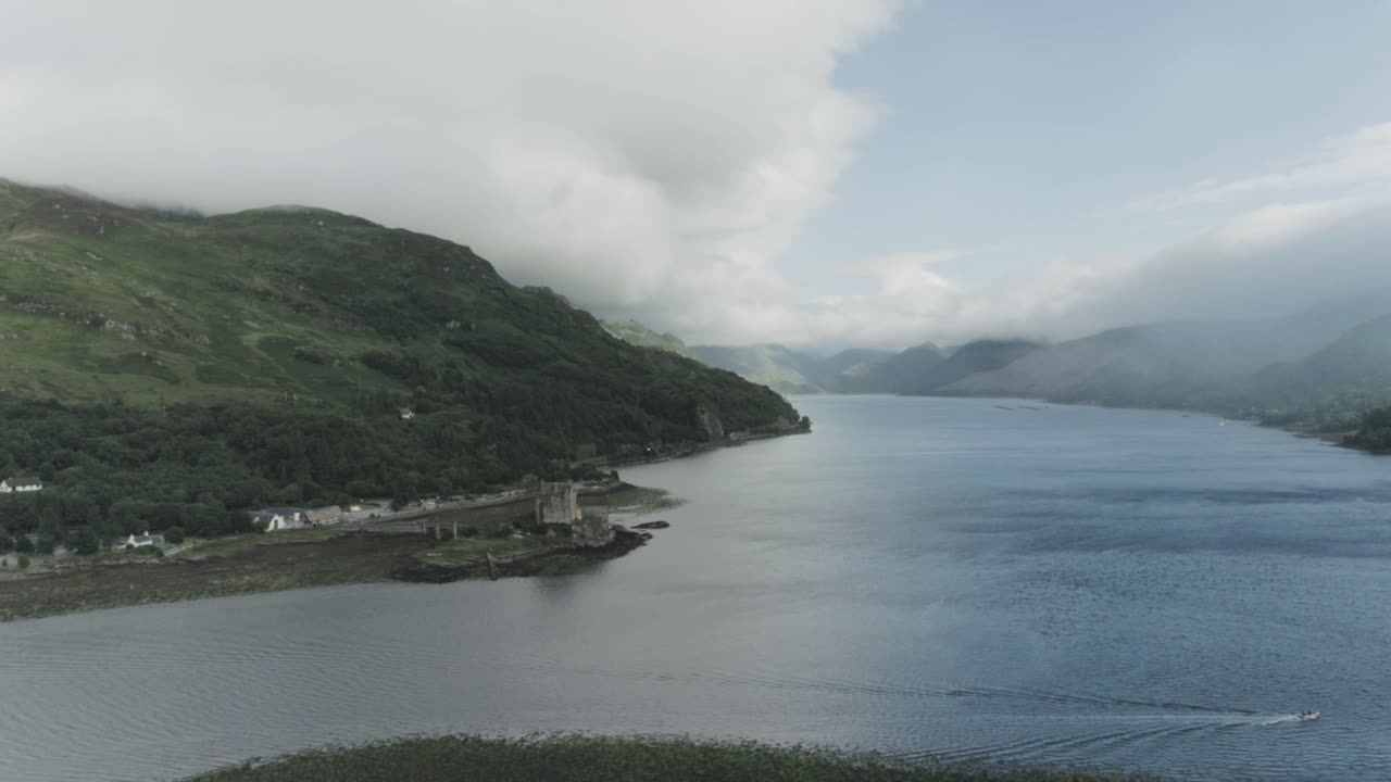 Super wide drone shot of Eilean Donan Castle moving backwards showing the vast mountain and sea view which surronds the castle in Scotland