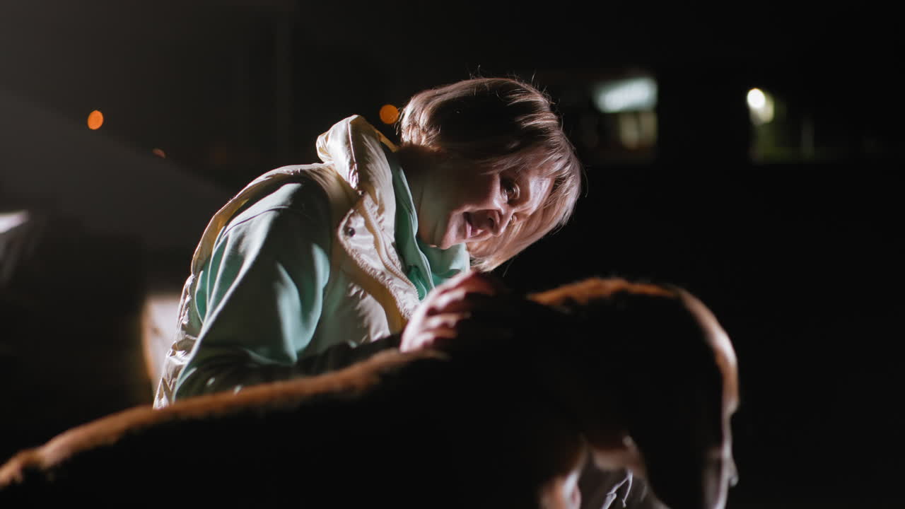 Sports lady seated with sport pet during nighttime training session, gently communicating and bonding with her loyal dog while illuminated softly against dark background, expressing affection