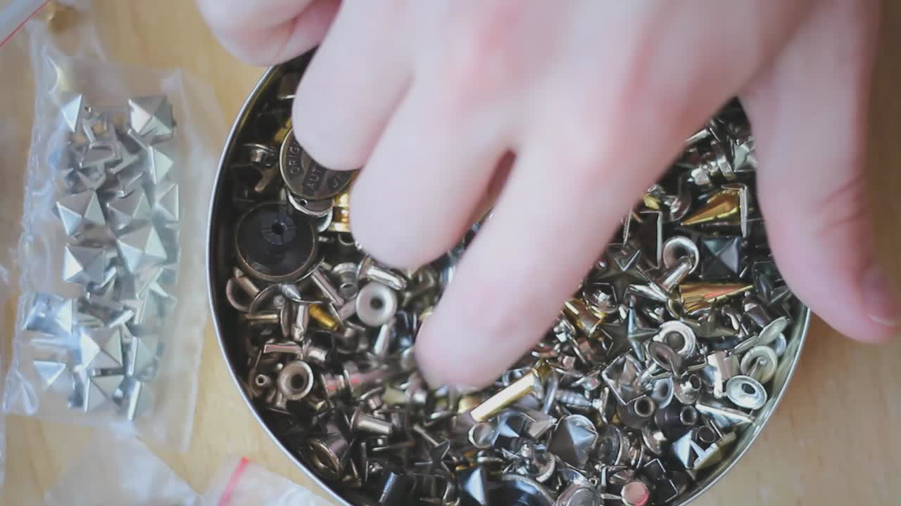 recogiendo a mano remaches y espárragos puntiagudos dorados y plateados de una caja con varios diferentes