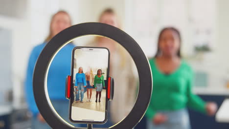 group of teenage girls in kitchen recording online dance video on mobile phone for social media