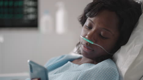 black woman patient in hospital with saline solution volumetric infusion pump using mobile phone on examination couch. african women lying in hospital bed with smart mobile phone while in hospital.