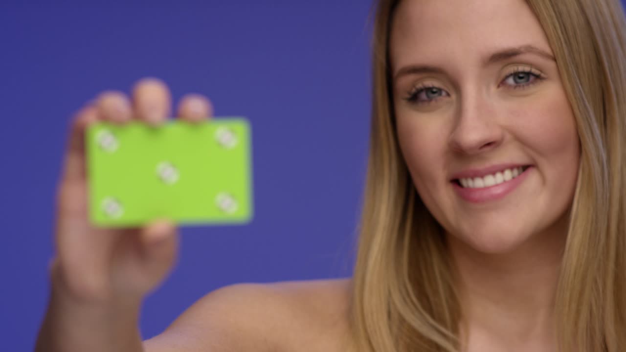 rack enfoque tiro de una hermosa mujer sosteniendo una tarjeta de crédito en blanco en la cámara