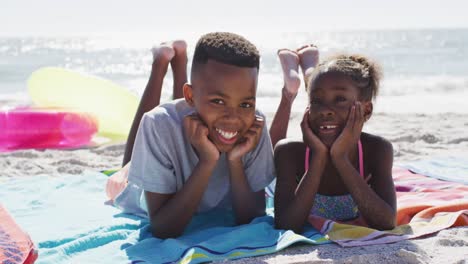 Video-Eines-Glücklichen-Afroamerikanischen-Geschwisterkindes,-Das-Auf-Einem-Handtuch-Am-Strand-Liegt