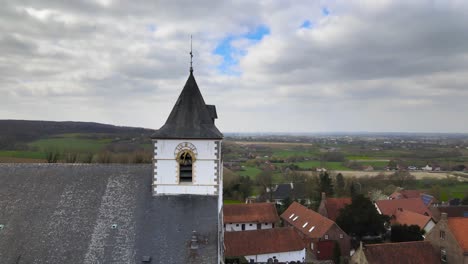 luftdrohne, die sich um die kirchenuhr dreht, mit belgischen hügeln im hintergrund