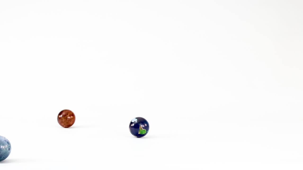 Small glass marbles and an Earth globe toy bounce and roll across a white surface