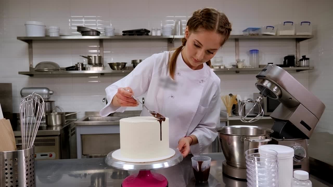 En konditor heller flytende sjokolade fra en skje på en hvit krembløtkake