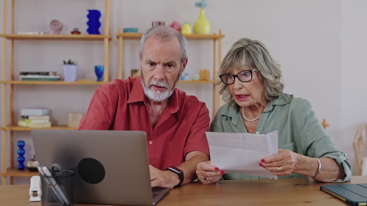 Concerned senior couple looking at bills on laptop
