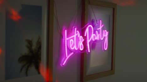 close up of neon let's party sign hanging on wall at house party