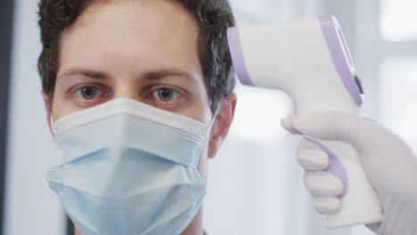 hombre con máscara facial midiendo su temperatura en la oficina