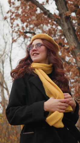 mujer elegante con boina amarilla y gafas de sol toca juguetón el silenciador mientras pasea por el bosque de otoño, disfrutando del aire fresco y las hojas coloridas en un entorno al aire libre sereno