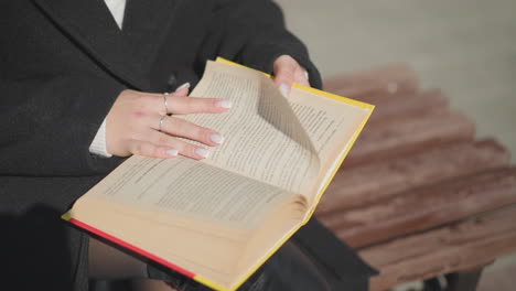 primer plano de las páginas del libro siendo giradas por una dama con uñas bien cuidadas adornadas con un anillo, mostrando la acción de la lectura en un día soleado con un efecto de fondo borroso suave