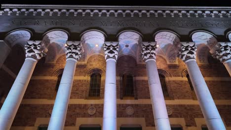 Toma-Fija-De-Alta-Calidad-Acercándose-Y-Mirando-Las-Columnas-Romanas-Iluminadas-Del-Edificio-De-La-Capital-Del-Estado-De-California-Por-La-Noche.