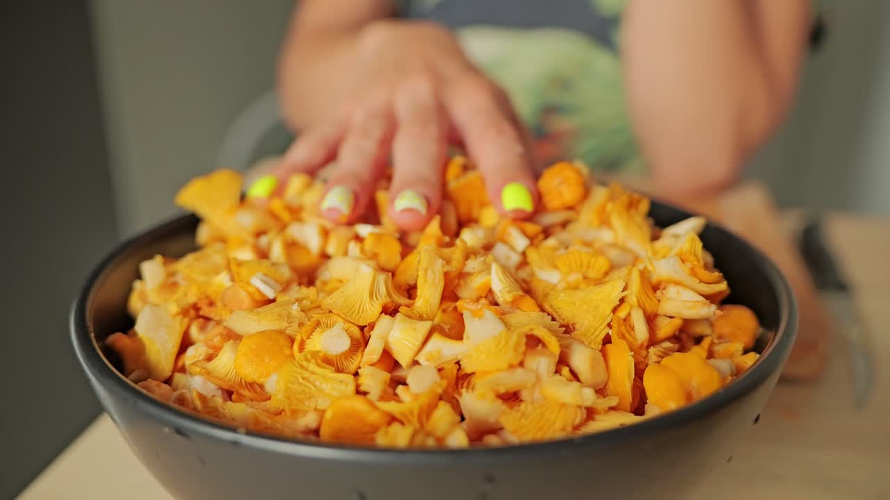 Hand glides sensually across golden chanterelles in bowl, evoking nature's bond