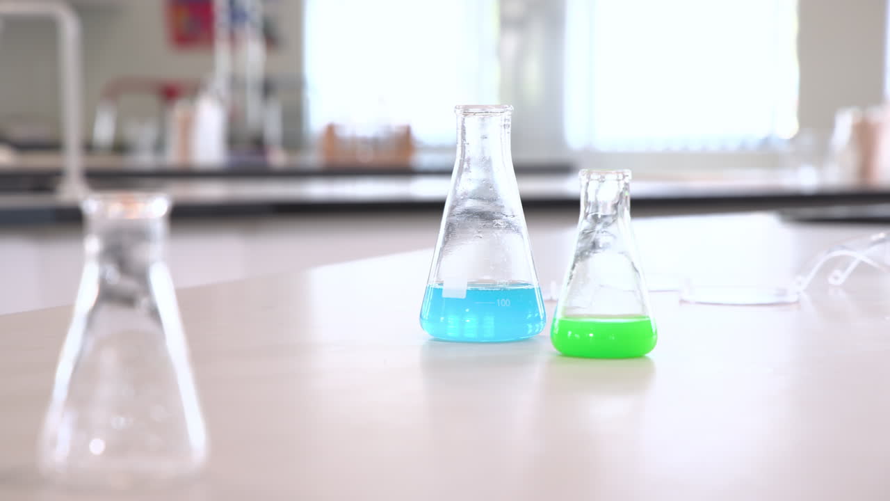 Colorful liquids in beakers on lab table in school science classroom, copy space