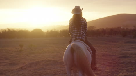 a young woman riding a horse on a ranch at sunset