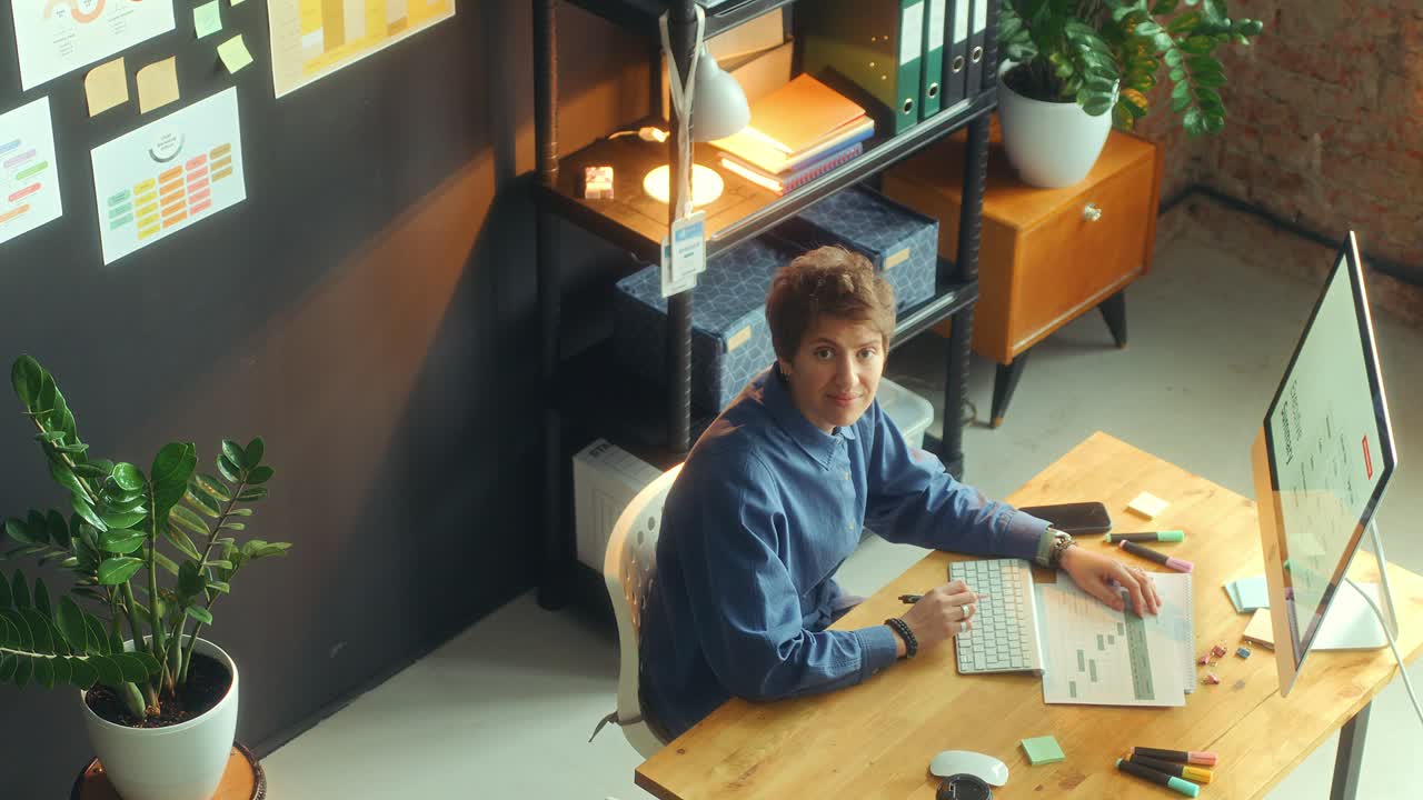 Junge Geschäftsfrau posiert vor der Kamera am Schreibtisch im Büro