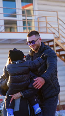 caucasian man in warm clothes walks outdoors. man comes up to his wife and baby and embraces them. vertical video.