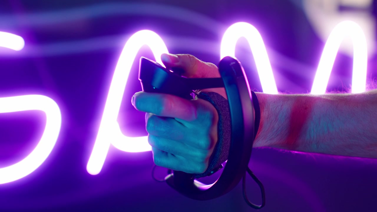 Primo piano di una mano che tiene un controller VR contro luci al neon