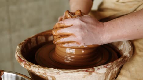 Spinning-pottery-wheel-close-up.-Foot-of-potter-in-black-pants-working-in-pottery-workshop.-Beautiful-young-woman-working-on-vase-in-pottery-master-class.-Close-up.-Unrecognizable-person