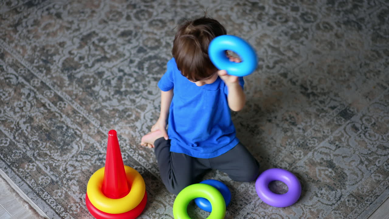 Little boy sits on the floor playing with a pyramid. Cute child playing peacefully at home. Top view.