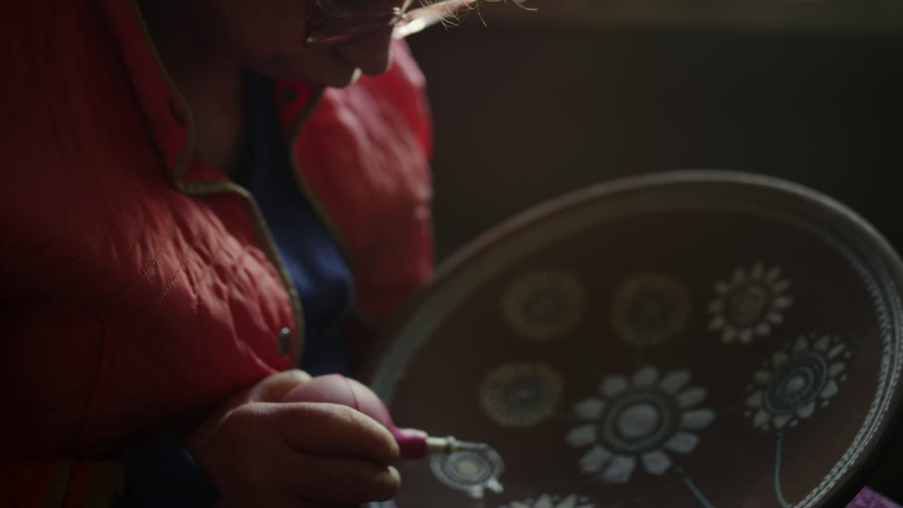 Focused woman decorating clay product in pottery. Female artist painting plate