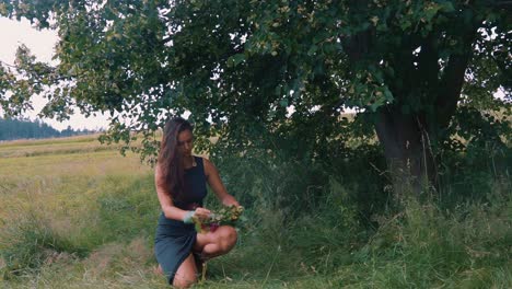 attractive girl in nature under tree making floral wreath, slow motion
